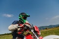 A professional motocross rider, fully geared up with helmet, gloves, and goggles, sitting poised on their motorcycle