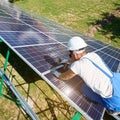 Professional mounter installing solar batteries on green metallic carcass.