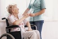 Nurse in a blue uniform gives a glass of water to an elderly woman in a wheelchair