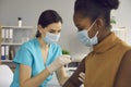 Nurse in medical face mask giving injection to patient during vaccination campaign