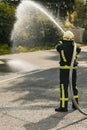 One young male firefighter on duty dressed in uniform with water hose sprinkling water