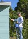 Professional painter or homeowner man on a ladder with paint can and brush painting the exterior of a residential house