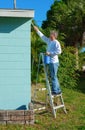 Professional painter or homeowner man on a ladder with paint can and brush painting the exterior of a residential house