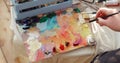 Professional paintress mixing oil paints on palette using brush, hand closeup.