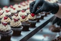 Professional pastry chef hands with black gloves decorating cupcakes with cream cheese cream and small red hearts Royalty Free Stock Photo