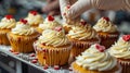 Professional pastry chef hands with white latex gloves decorating cupcakes with cream and red hearts. Royalty Free Stock Photo