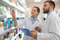 Professional pharmacists near shelves in drugstore