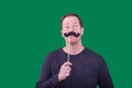 Adult man looking up holding a fake black mustache to his face photographed on green screen background Royalty Free Stock Photo