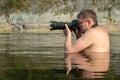 A professional photographer with glasses sits on a mountain river in front of his chest and holds a digital camera in his hands. A Royalty Free Stock Photo