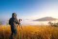 Professional photographer taking a photo with camera lens and tripod on top of mountain with meadow and cloud fog landscape with Royalty Free Stock Photo