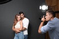 Professional photographer taking picture of young couple on dark grey background