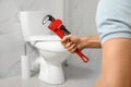 Professional plumber holding pipe wrench near toilet bowl in bathroom Royalty Free Stock Photo