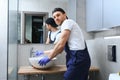 Professional plumber, male worker in uniform installing sink and water pipe in new apartment.