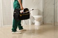 Professional plumber with toolbox near toilet bowl in bathroom, closeup