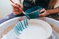 Professional potter works on painting plates in the workshop. Woman paints a ceramic plate with a brush and blue paint Royalty Free Stock Photo