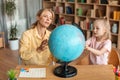 Professional preschool teacher teaching cute girl about globe, having private home class, sitting at desk in living room Royalty Free Stock Photo