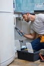 Professional repairman looking focused, using pipe wrench while examining and fixing sink pipe in the kitchen