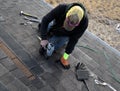 Professional roofer uses a nail gun to fix new shingles.