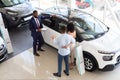 Professional Salesman Advertising New Car For Young Black Customers Couple In Showroom Royalty Free Stock Photo