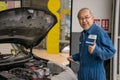 Professional senior car mechanic giving thumb up near automobile working in the garage workshop