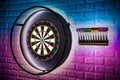 Professional sisal steeldart board with steel dart holder in colorful LED illumination white stone wall. leisure time hobby sport Royalty Free Stock Photo