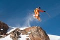 A professional skier makes a jump-drop from a high cliff against a blue sky leaving a trail of snow powder in the Royalty Free Stock Photo