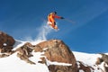 A professional skier makes a jump-drop from a high cliff against a blue sky leaving a trail of snow powder in the Royalty Free Stock Photo