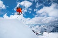 A professional skier in an orange suit jumps from a high cliff against a background of blue sky and clouds, leaving a Royalty Free Stock Photo