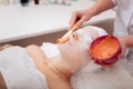 Professional skilled cosmetologist applying an orange mask