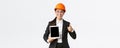 Professional smiling asian female construction manager, factory engineer in business suit and safety helmet showing
