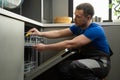 Repairman checks operating state of dishwasher in kitchen