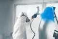 Professional spray painter in protective mask and clothes spraying car hood of vehicle part to blue color using spray Royalty Free Stock Photo