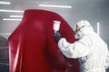 Professional spray painter in protective mask and clothes spraying car hood of vehicle part to red color using spray gun Royalty Free Stock Photo
