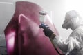 Professional spray painter worker applies finishing layer of varnish on purple car hood after main painting in car