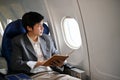 Successful Asian businessman holding a book while looking out the window, rduring the flight Royalty Free Stock Photo