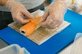 Professional sushi chef preparing roll at commercial kitchen. Cook puts the salmon on roll. Japanese cuisine recipes Royalty Free Stock Photo