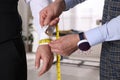 Professional tailor measuring client`s wrist circumference in atelier, closeup