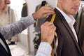 Professional tailor measuring shoulder seam length on client`s jacket in atelier, closeup Royalty Free Stock Photo