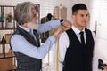 Professional tailor measuring shoulder seam length on client`s vest in atelier Royalty Free Stock Photo