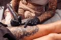Professional tattoo master creating artistic masterpiece on female thigh