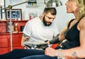 Professional bearded tattooer preparing blond woman for special tattoo session inside ink trendy studio - Skin fashion concept -