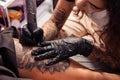 Professional tattooist creating black and white flower design on female thigh