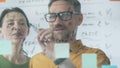 Professional team members brainstorming strategy, writing notes on transparent whiteboard with colorful sticky papers Royalty Free Stock Photo
