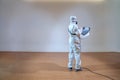 Professional technical man in prevention suit sprays sterilising solution by electrical spray machine on wood floor and white
