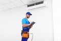 Professional technician with clipboard near modern air conditioner