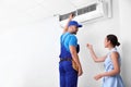 Professional technician speaking with woman about air conditioner indoors