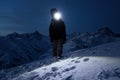 Professional tourist climb on snowy mountain at night and lights the way with a headlamp. Snowboarder walking in front of amazing