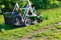 A professional tractor mower driven by a public utility worker climbs up the slope and mows tall grass