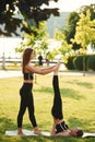 Professional trainer is helping. Two women in sport clothes are doing exercises outdoors on the field