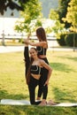 Professional trainer is helping. Two women in sport clothes are doing exercises outdoors on the field